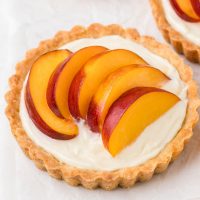 Close-up photo of a peach tartlet that is topped with juicy sliced peaches.