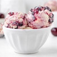 Image of a white bowl full of creamy black cherry ice cream with cherry preserves swirled through the ice cream with bits of cherries