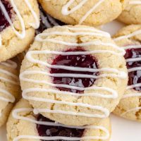 Photo of several raspberry thumbprint cookies scattered on a white background showing the raspberry center with striped glaze