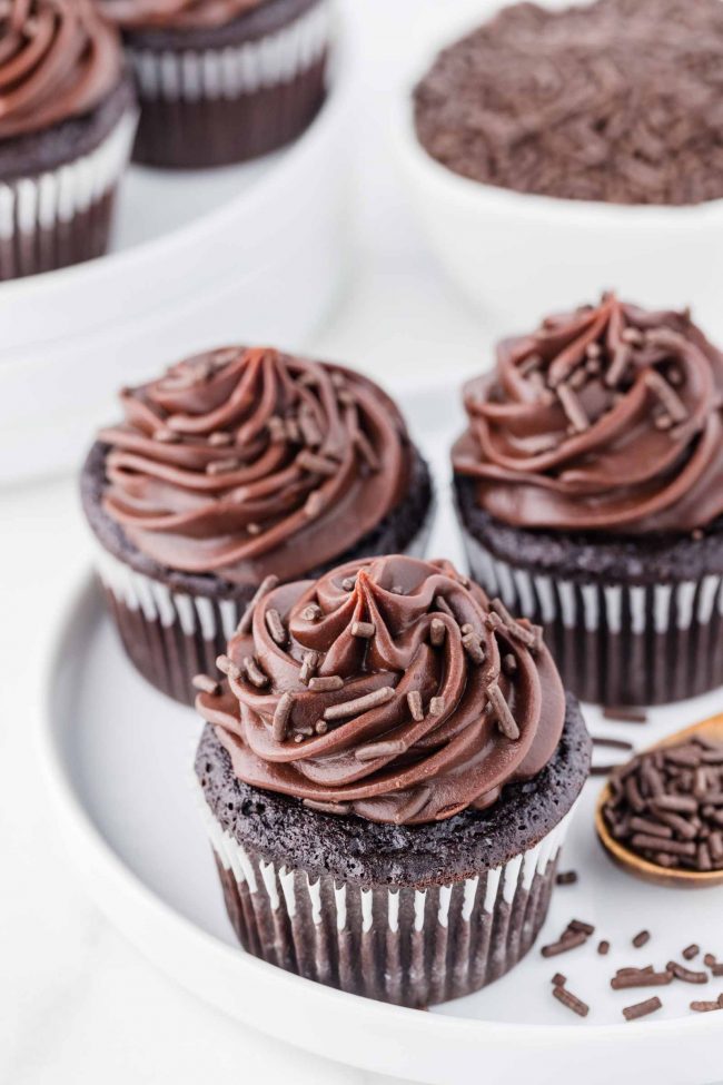 Eggless cupcakes with chocolate frosting and sprinkles on a white cake stand