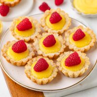 lemon tartlets on a white plate and topped with raspberries